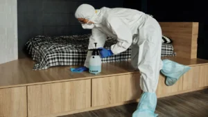 Professional technician in white protective coveralls spraying bio-mist sanitizer in a bedroom