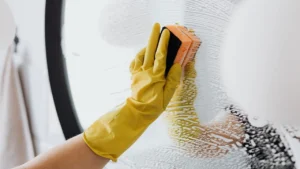 Professional cleaner in gloves wiping bathroom tile grout to restore white color