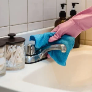 Professional cleaner polishing bathroom chrome fixtures to prepare for landlord inspection