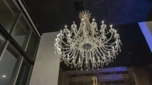 Professional technician on a tall A-frame ladder dusting a luxury crystal chandelier in a villa foyer