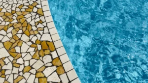 Professional patio cleaner pressure washing outdoor stone tile flooring next to a swimming pool